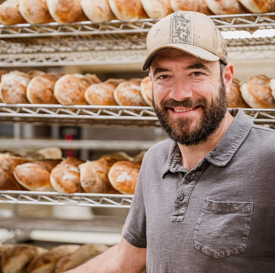 Second-generation owner standing in front of the bakery's fresh bread racks